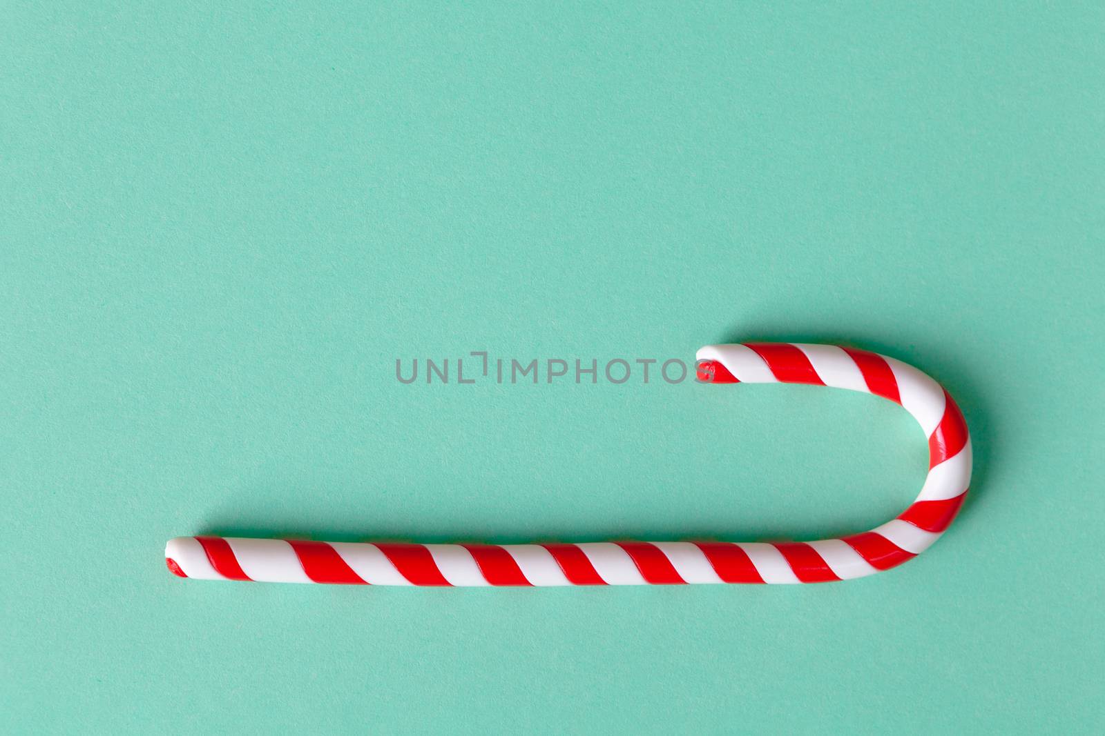 Christmas peppermint candy cane on pastel turquoise background. Festive minimal style flat lay. Mockup with copy space for greeting card, invitation, social media. Horizontal.