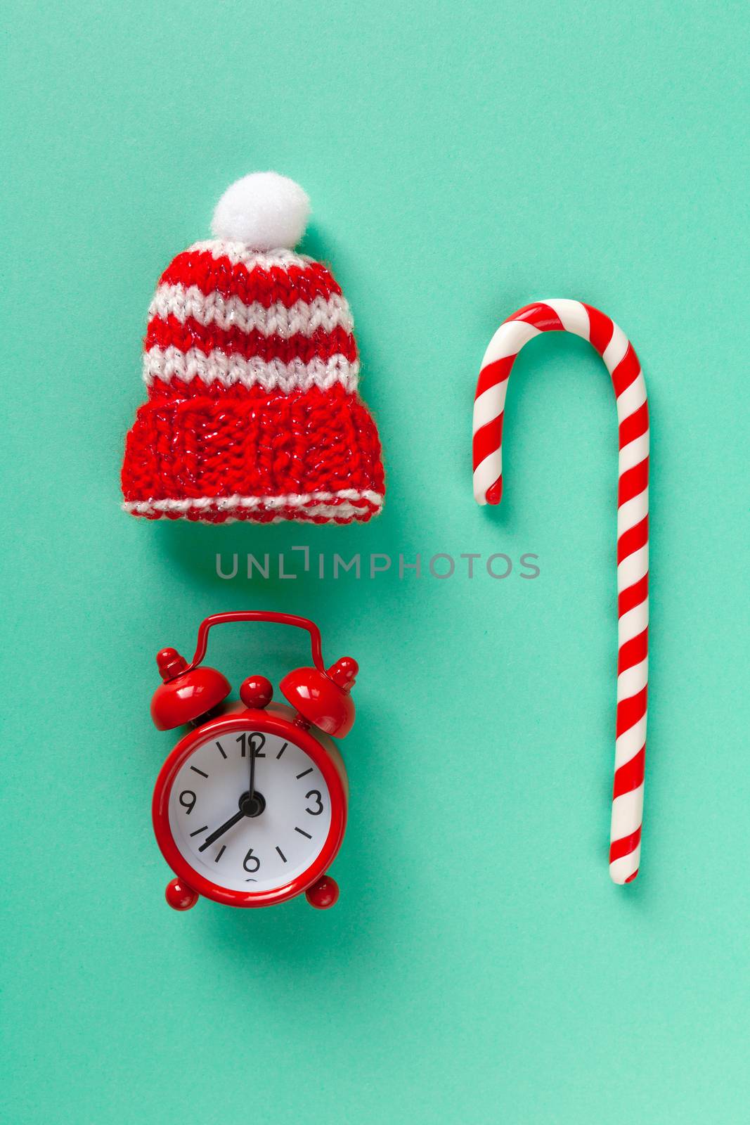 Christmas candy cane, clock and hat on pastel turquoise backdrop. Winter minimalistic flat lay. Vertical. Top view. Still life. Waiting for the holiday. Close-up, top view.