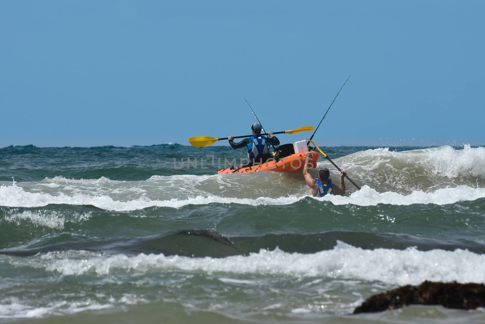 Two eager fishermen attempt to launch their ocean kayak in the waves, Mossel Bay, South Africa