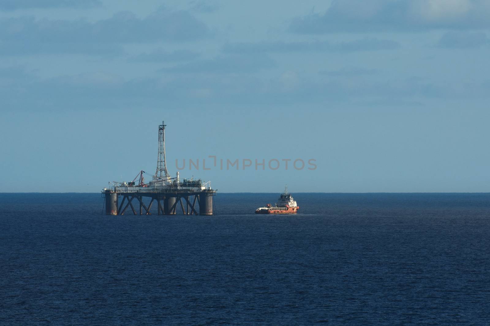 Oil drilling platform with a red service boat on open ocean, South Africa