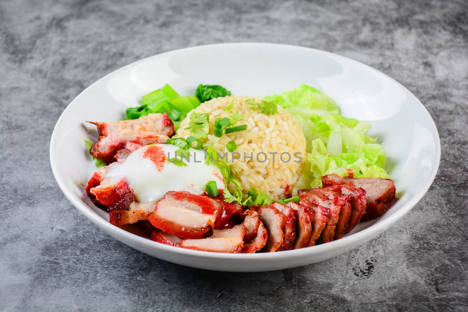 Barbecued red pork and crispy pork in red sauce, served with rice and vegetable on white plate.
