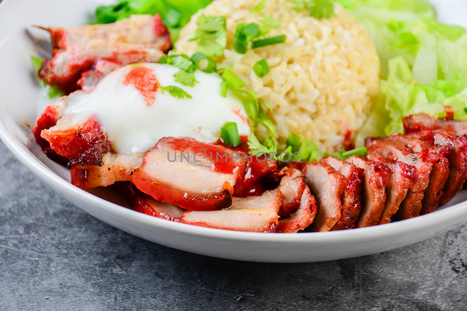 Barbecued red pork and crispy pork in red sauce, served with rice and vegetable on white plate.
