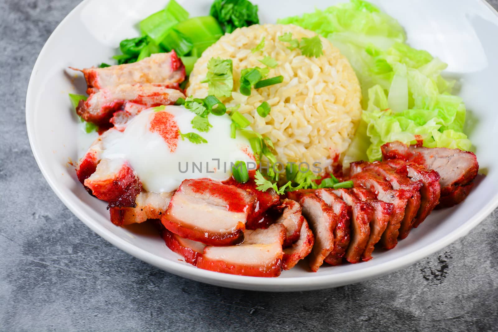 Barbecued red pork and crispy pork in red sauce, served with rice and vegetable on white plate.
