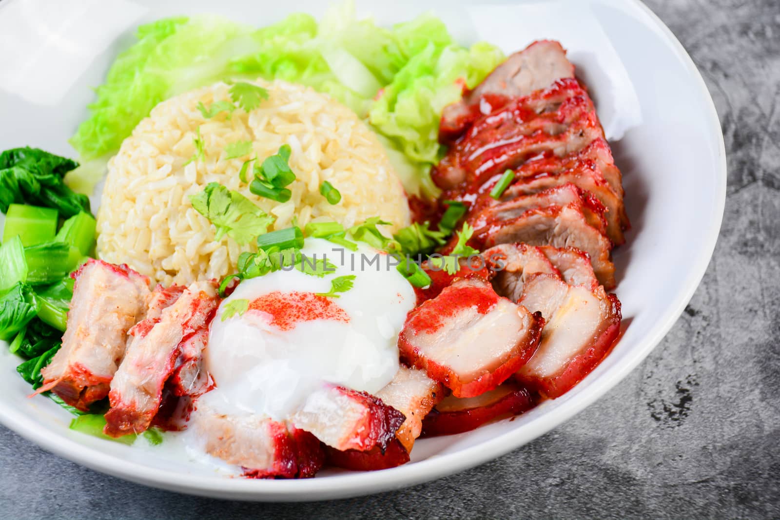 Barbecued red pork and crispy pork in red sauce, served with rice and vegetable on white plate.
