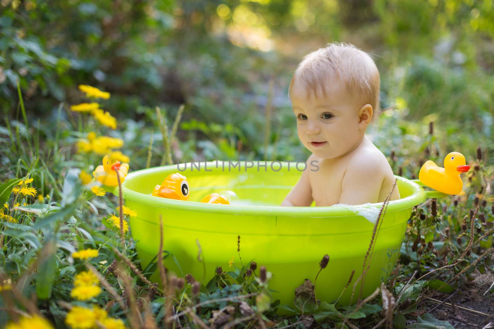 Cute toddler boy in basin taking a bath with bubbles and duck toys outdoor