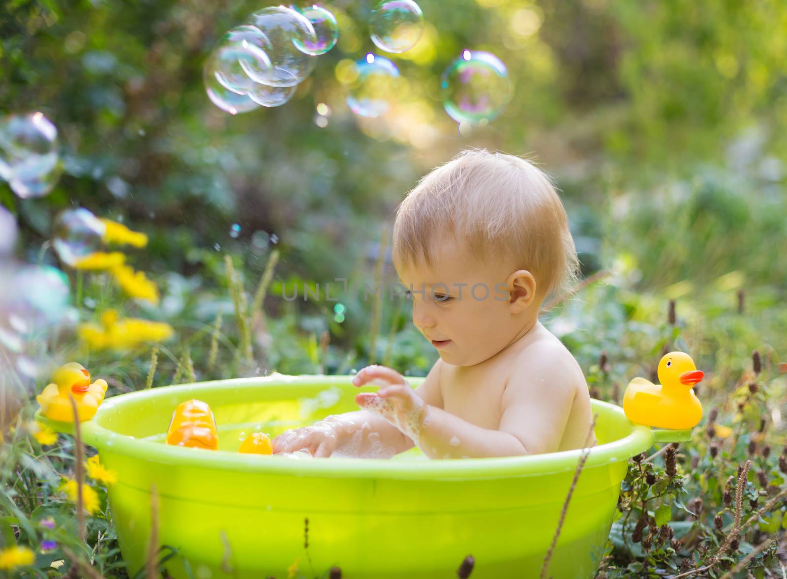 Cute little toddler boy in basin taking a bath with bubbles and duck toys outdoor