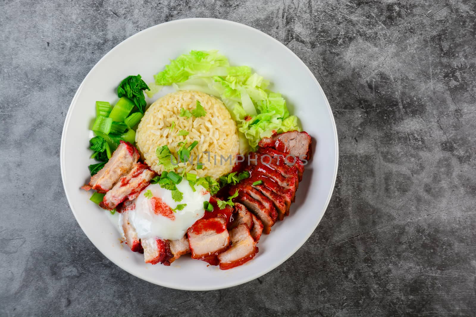 Barbecued red pork and crispy pork in red sauce, served with rice and vegetable on white plate.
