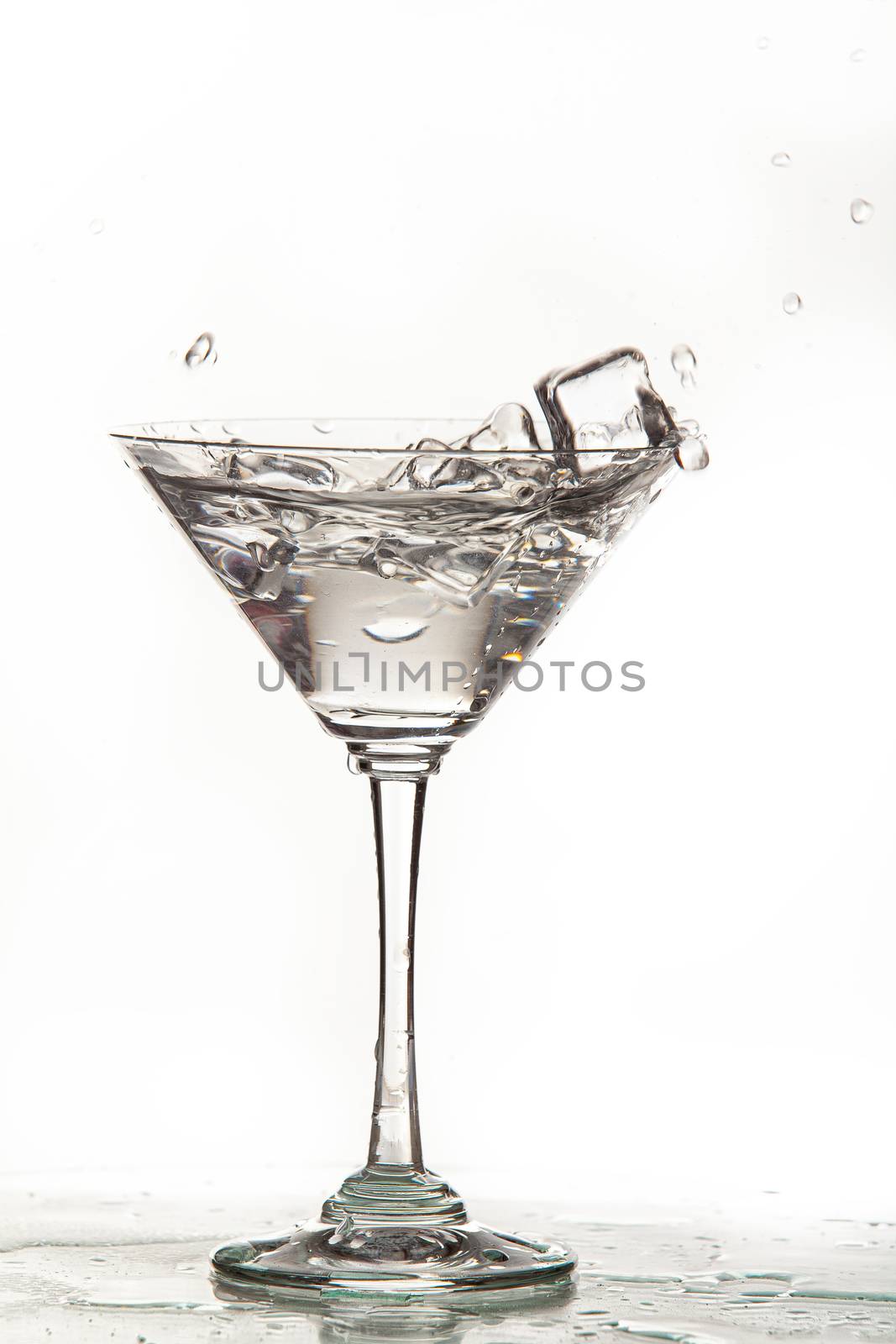 Glass, crystals of ice and pouring water on isolated studio background