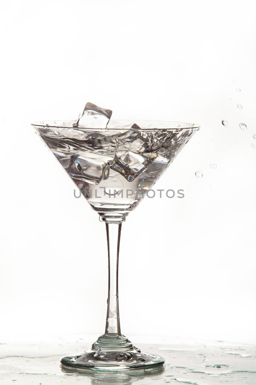 Glass, crystals of ice and pouring water on isolated studio background