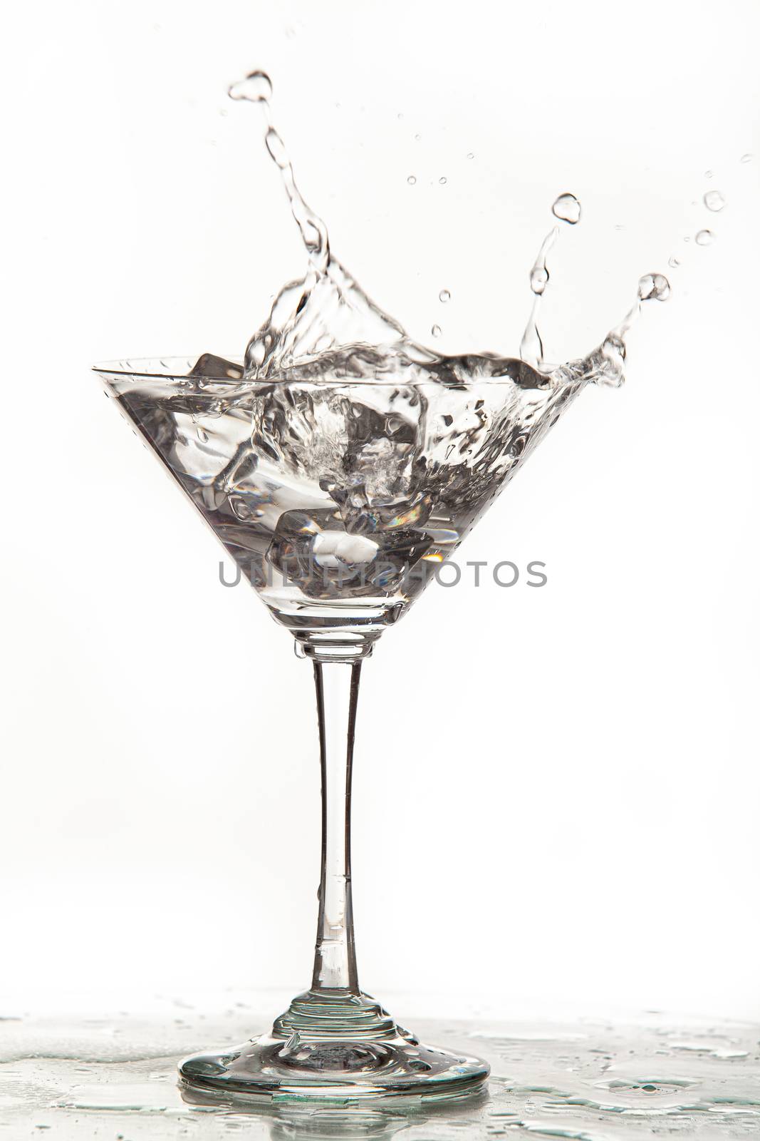 Glass, crystals of ice and pouring water on isolated studio background