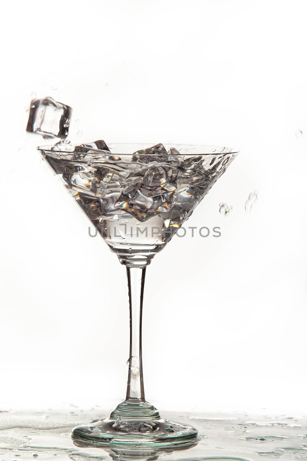Glass, crystals of ice and pouring water on isolated studio background