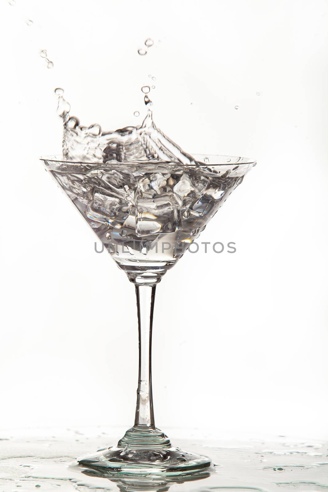 Glass, crystals of ice and pouring water on isolated studio background