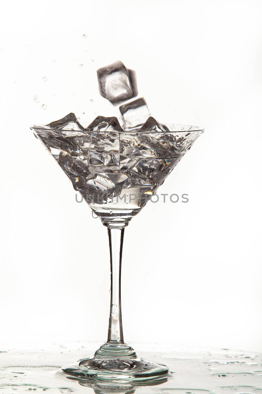 Glass, crystals of ice and pouring water on isolated studio background