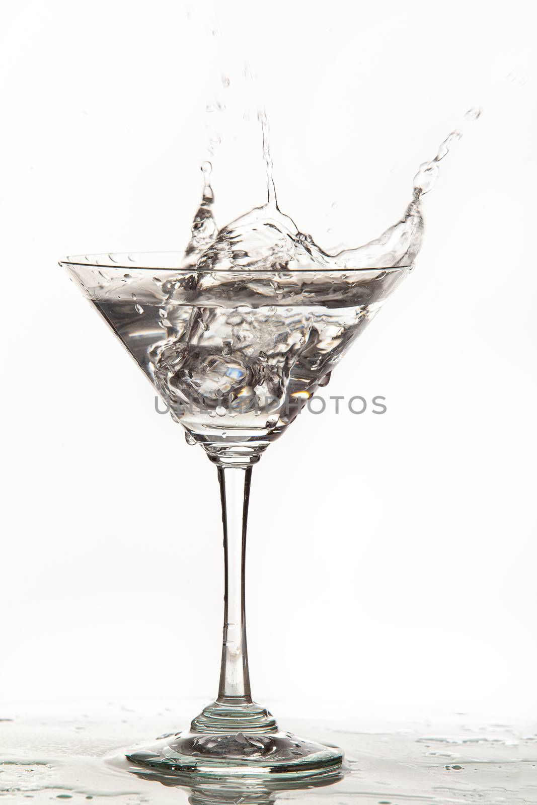 Glass, crystals of ice and pouring water on isolated studio background