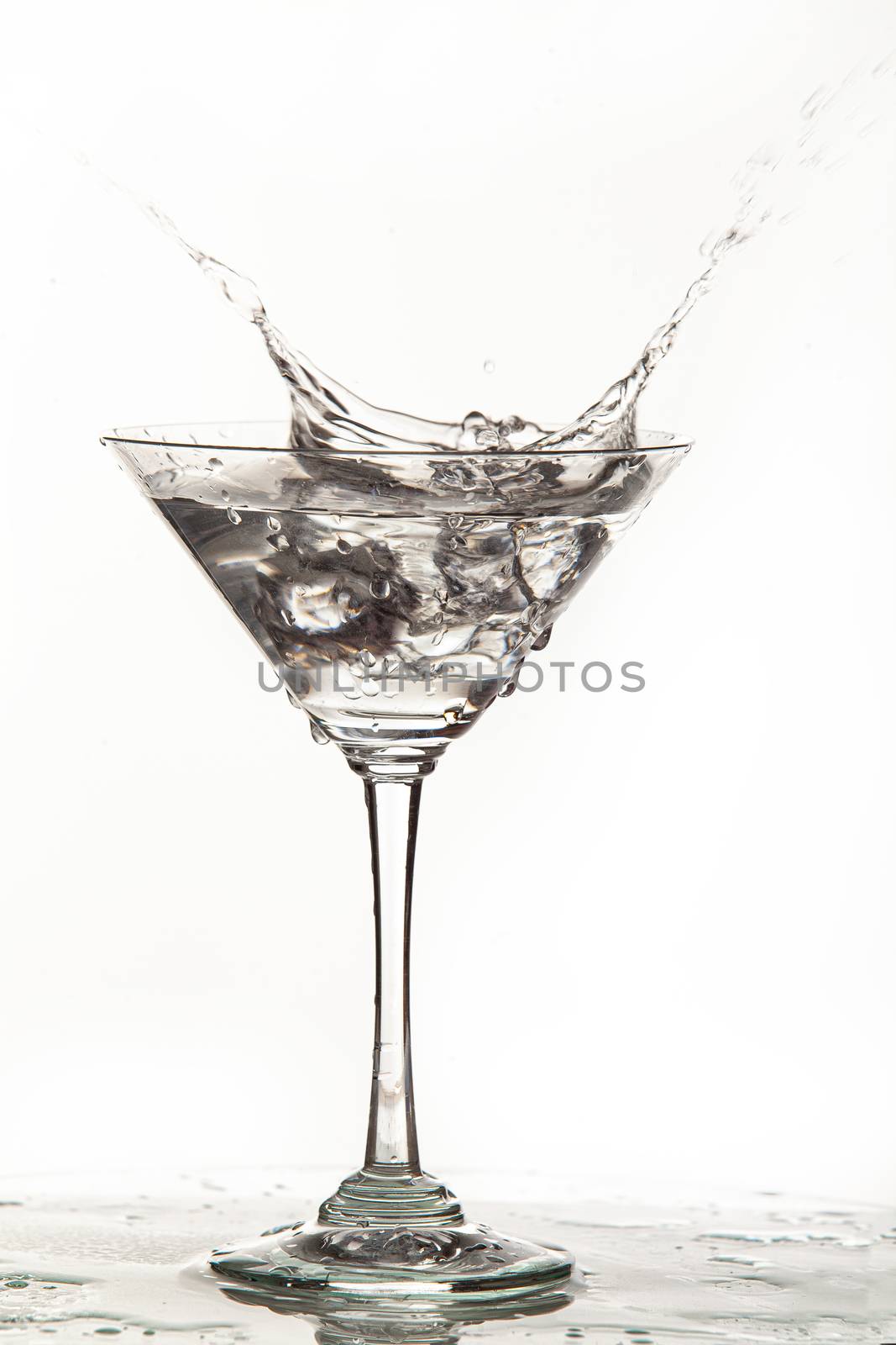 Glass, crystals of ice and pouring water on isolated studio background