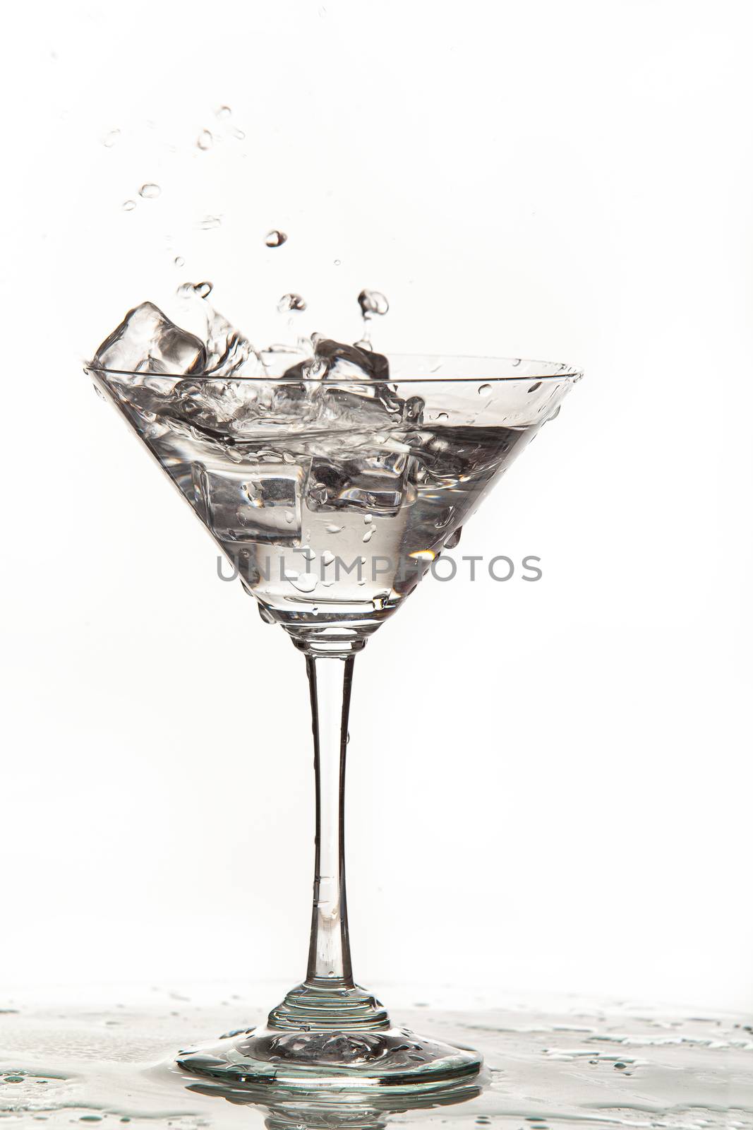 Glass, crystals of ice and pouring water on isolated studio background