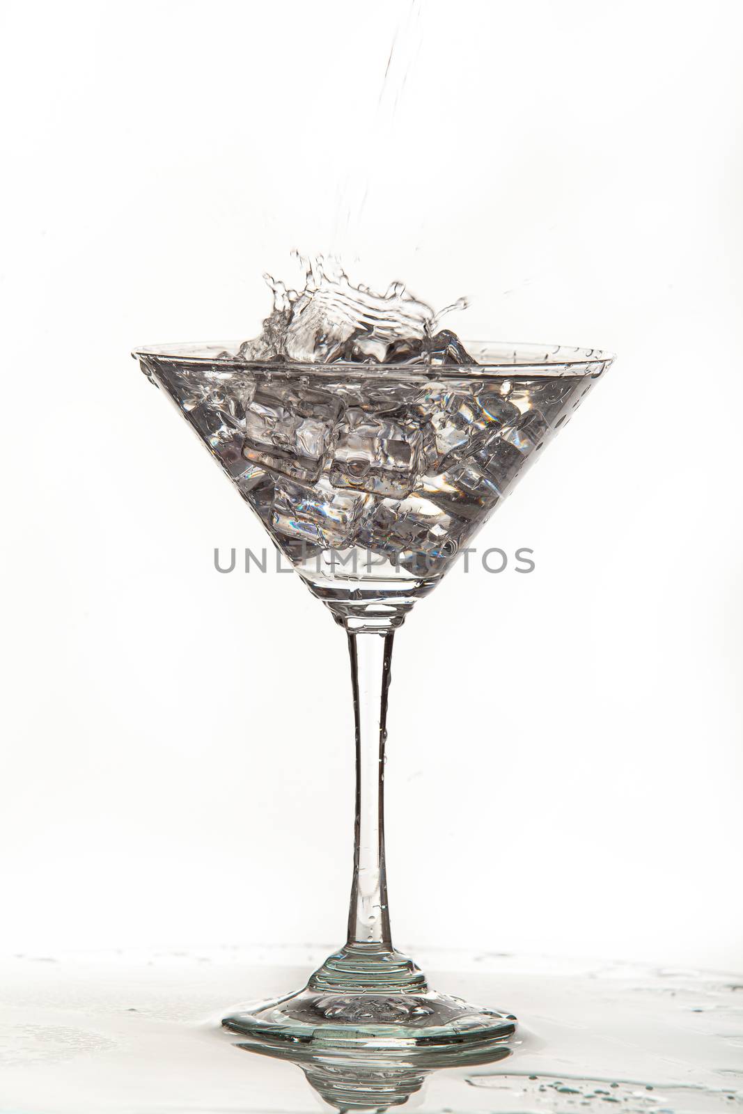 Glass, crystals of ice and pouring water on isolated studio background