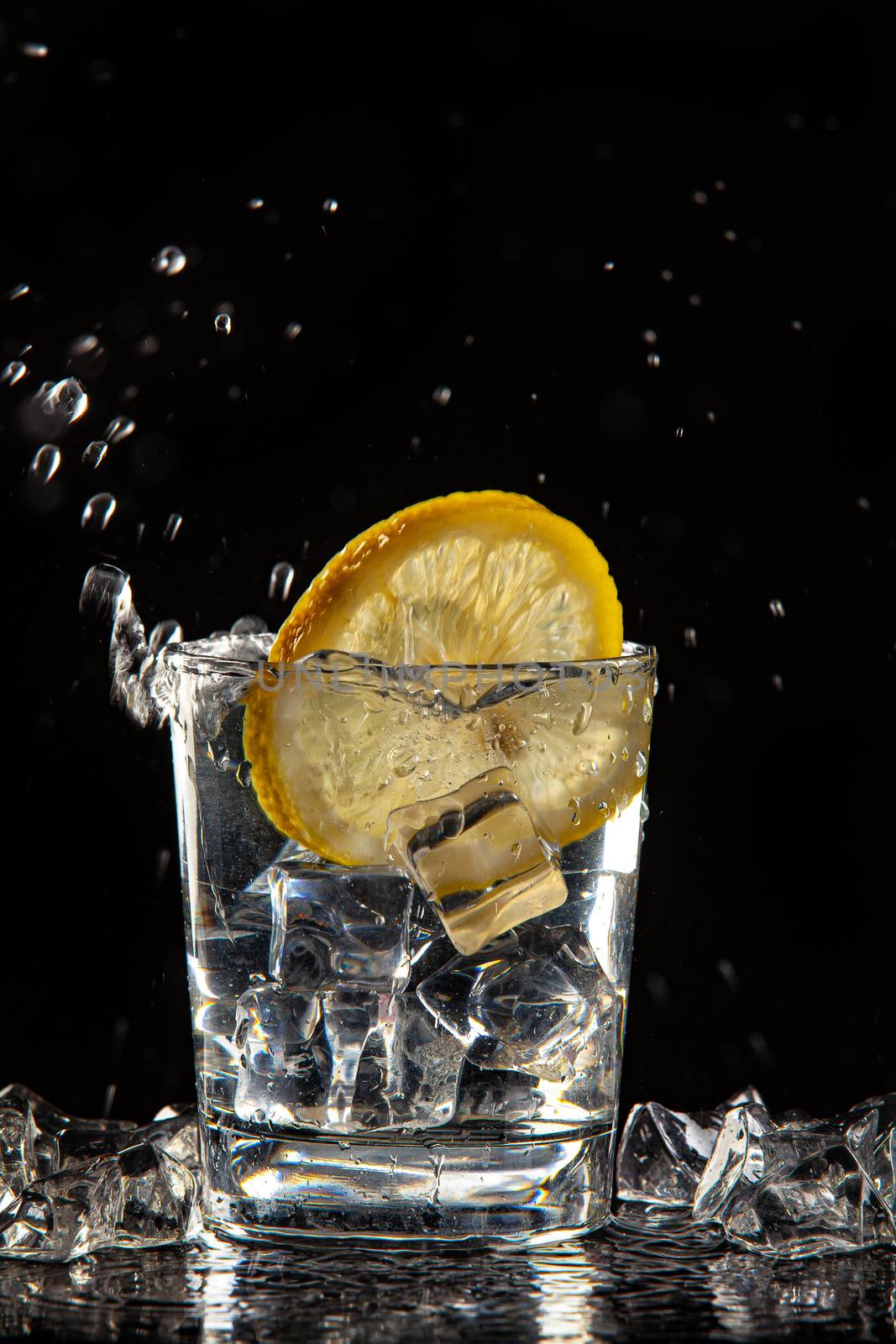 Glass of water, ice crystals and lemon on a black studio background