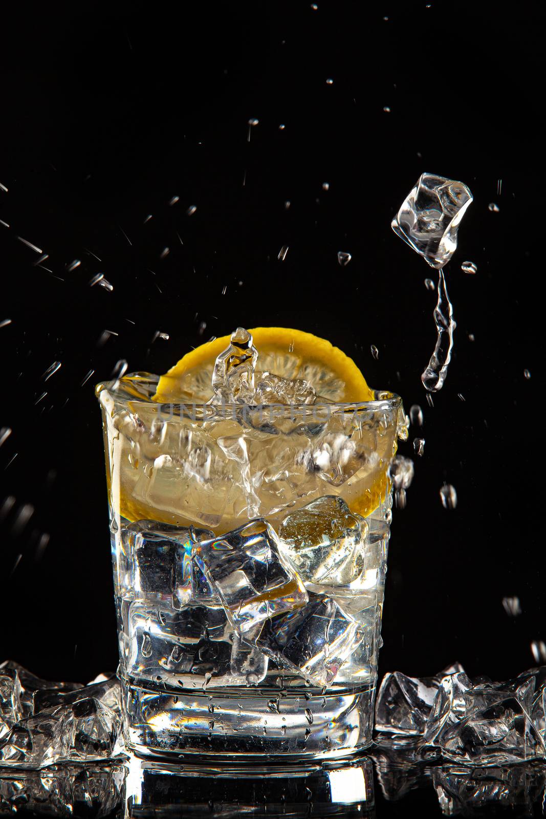 Glass of water, ice crystals and lemon on a black studio background