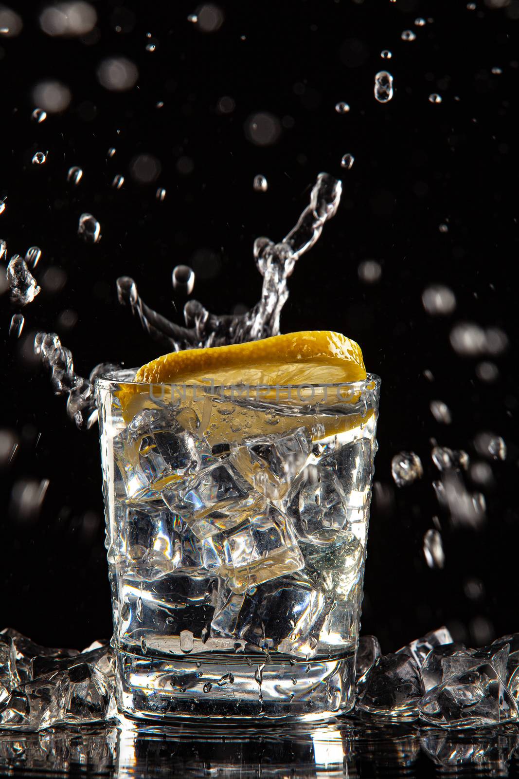 Glass of water, ice crystals and lemon on a black studio background
