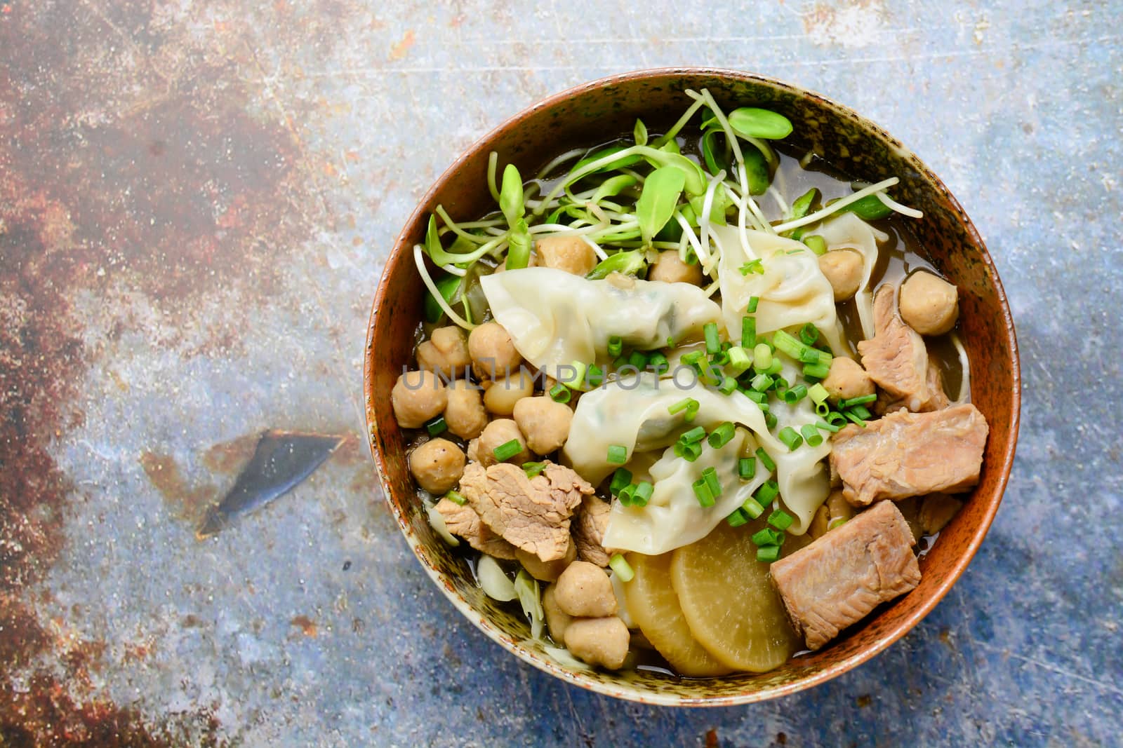 Wonton soup with meat balls, spring onion served in a big brown bowl, selective focus
