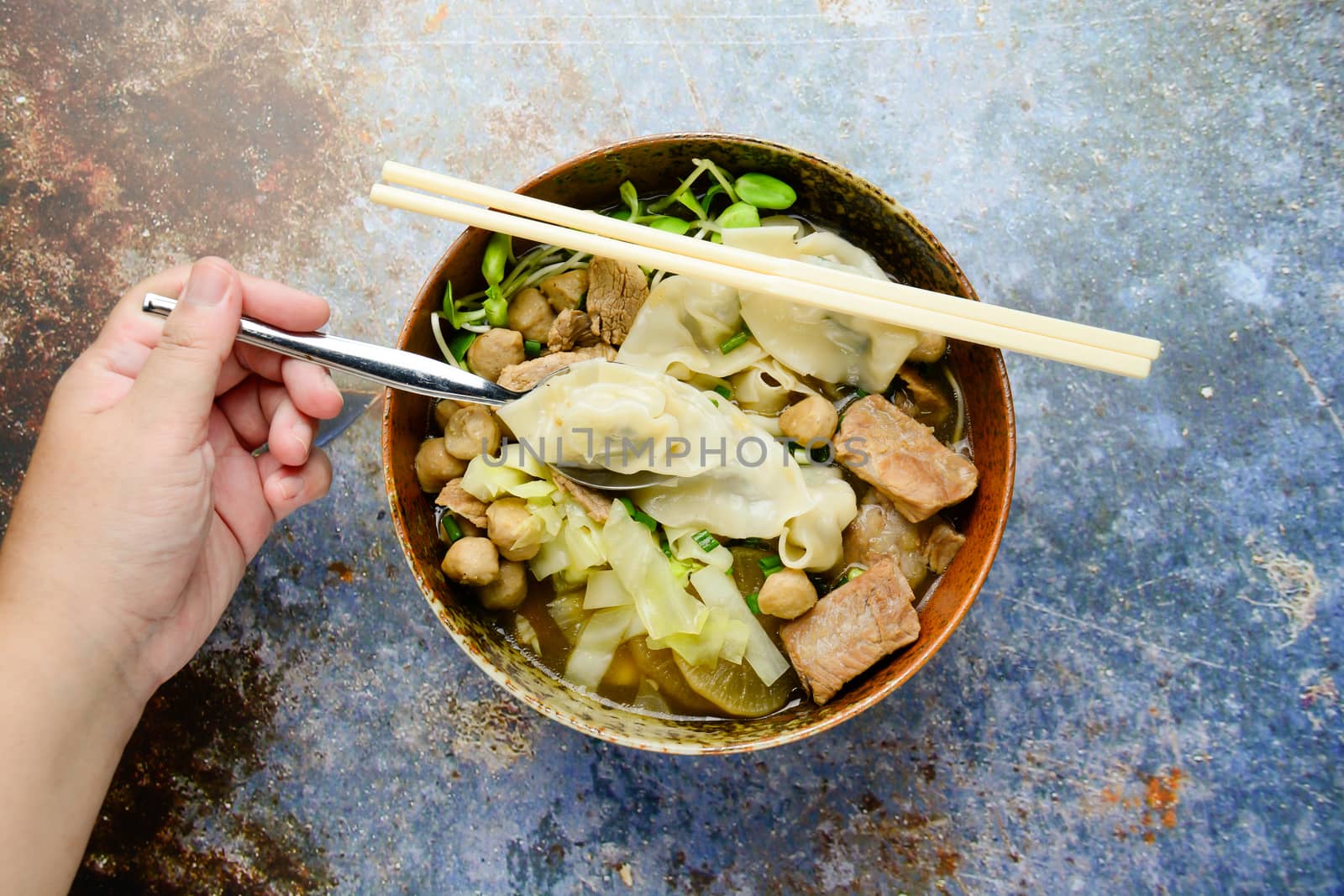 Wonton soup with meat balls, spring onion served in a big brown bowl, selective focus
