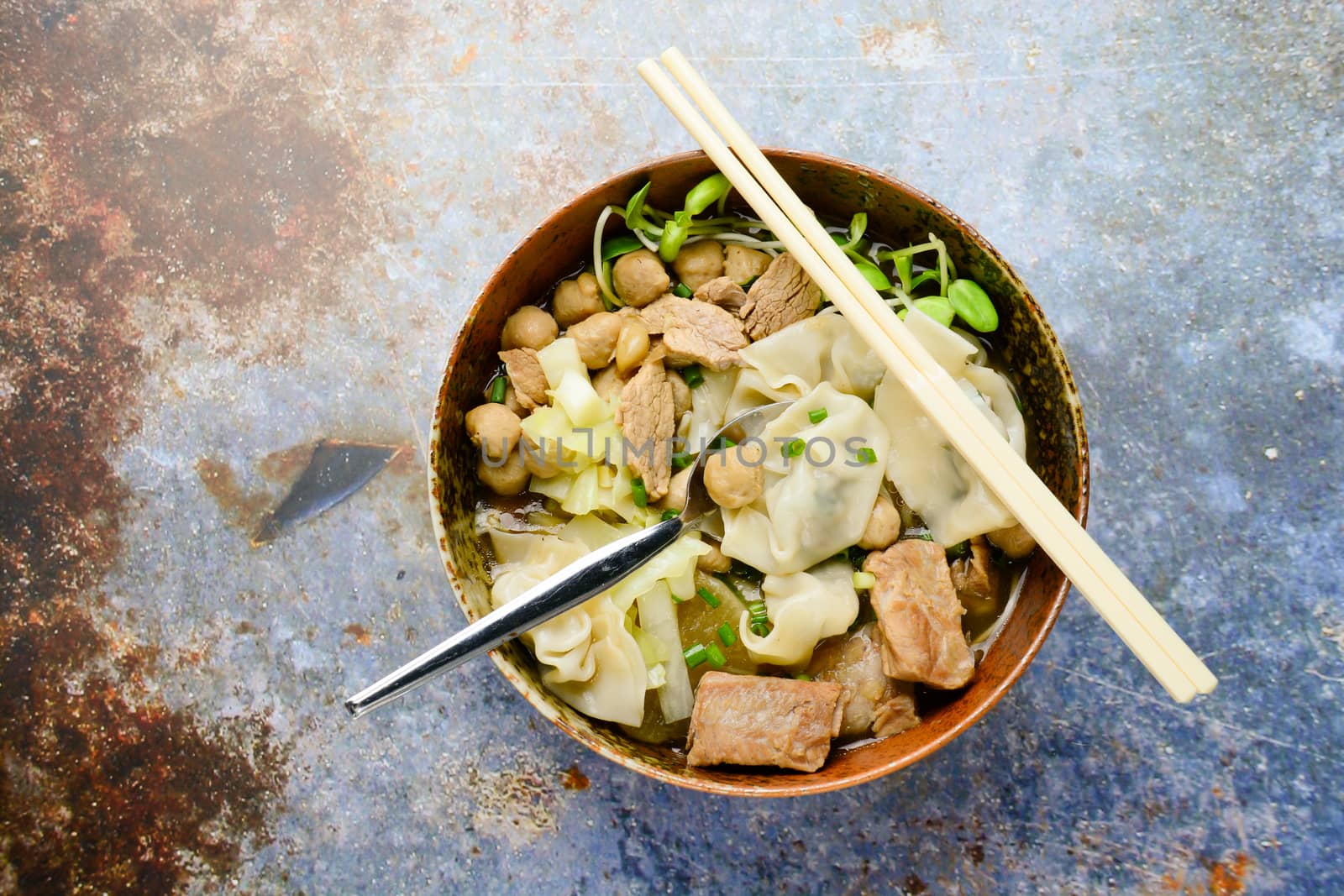 Wonton soup with meat balls, spring onion served in a big brown bowl, selective focus
