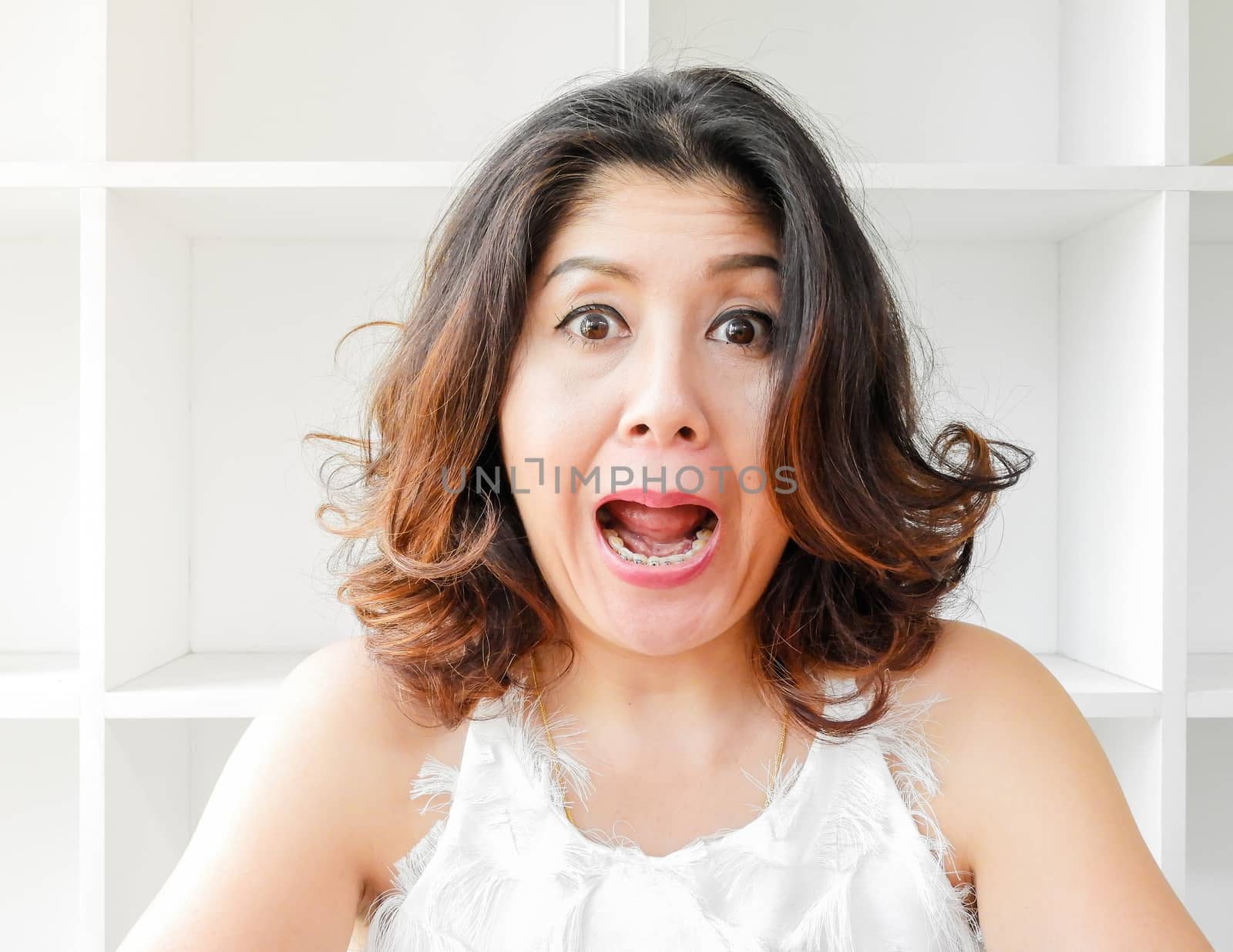 Close up portrait of a beautiful woman smiling, with white bookshelf background.
