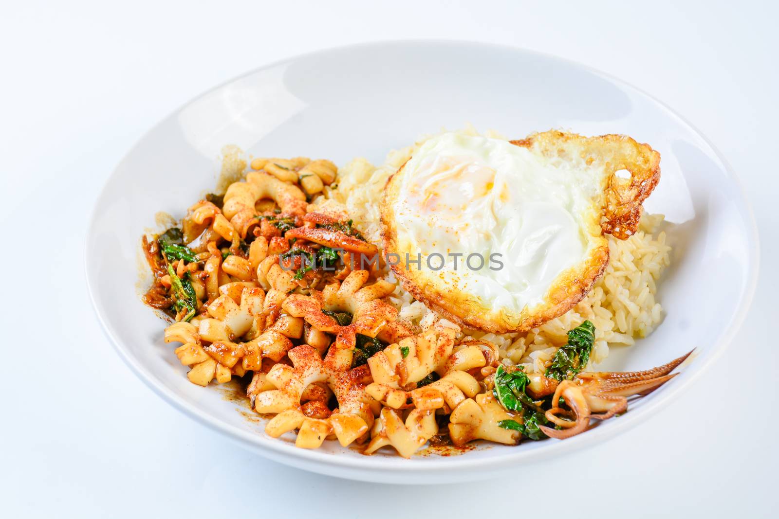 Spicy stir fried squid with basil leaves and chili, Sunny side up egg, served with brown rice. Hot and spicy dish.