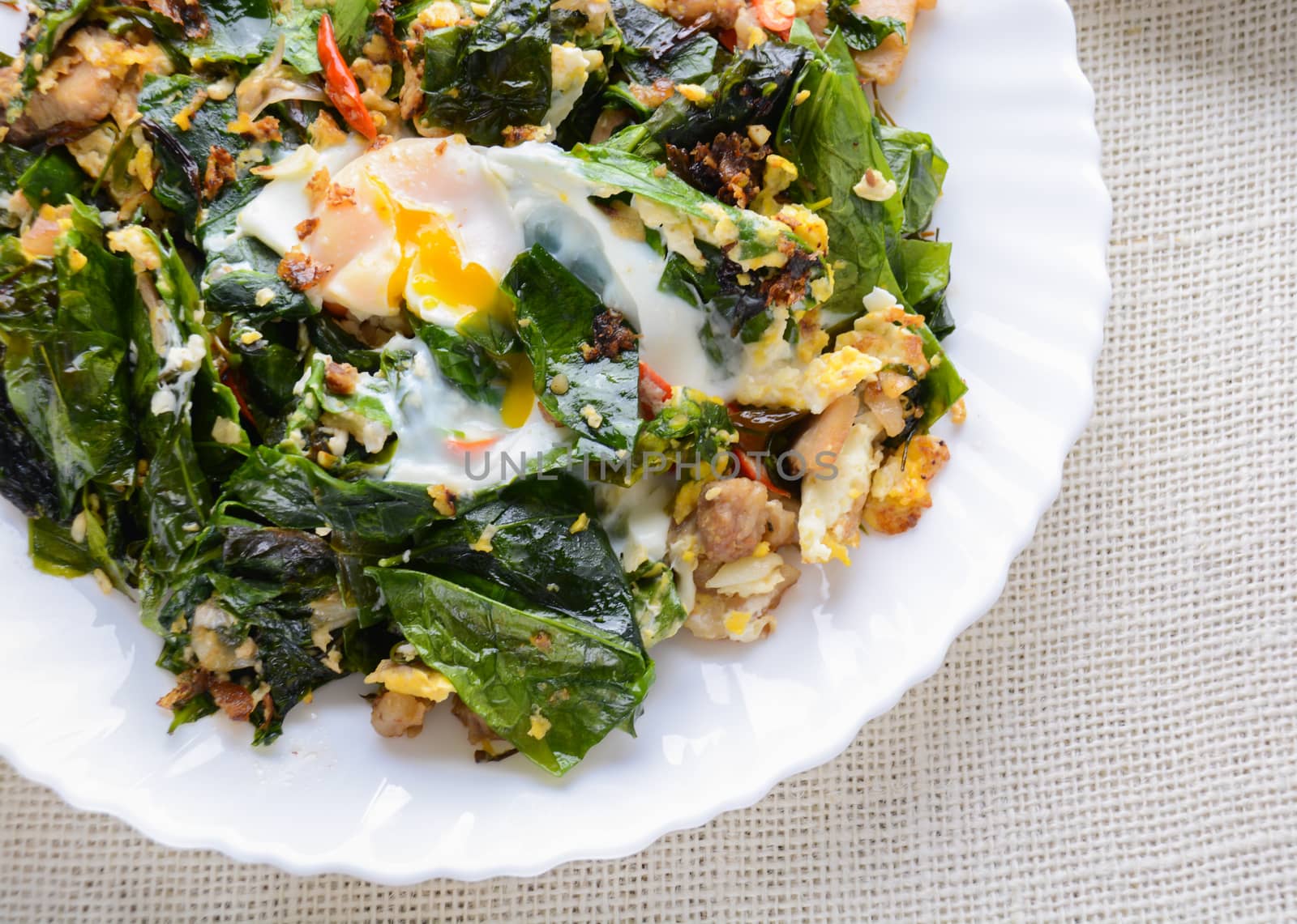 A white plate of delicious Stir-Fried Baegu Leaves or Melinjo with Eggs, served with steamed rice.