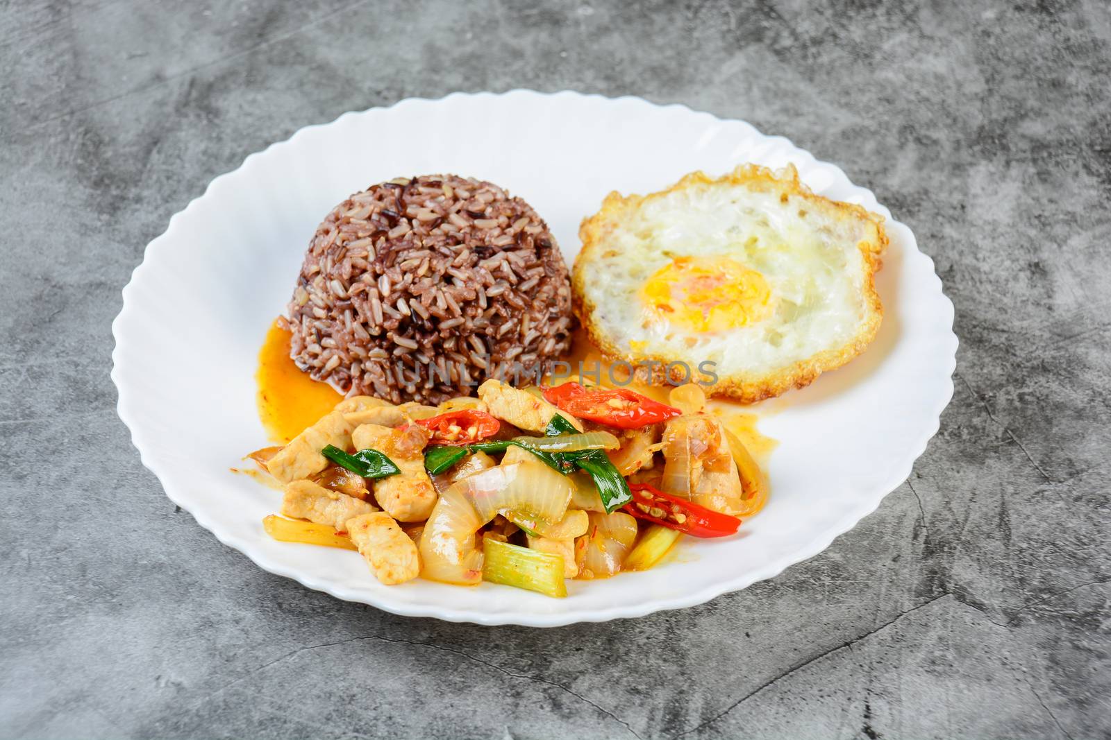 Stir fry chicken sweet onion and peppers, served with brown rice and fried egg on white plate
