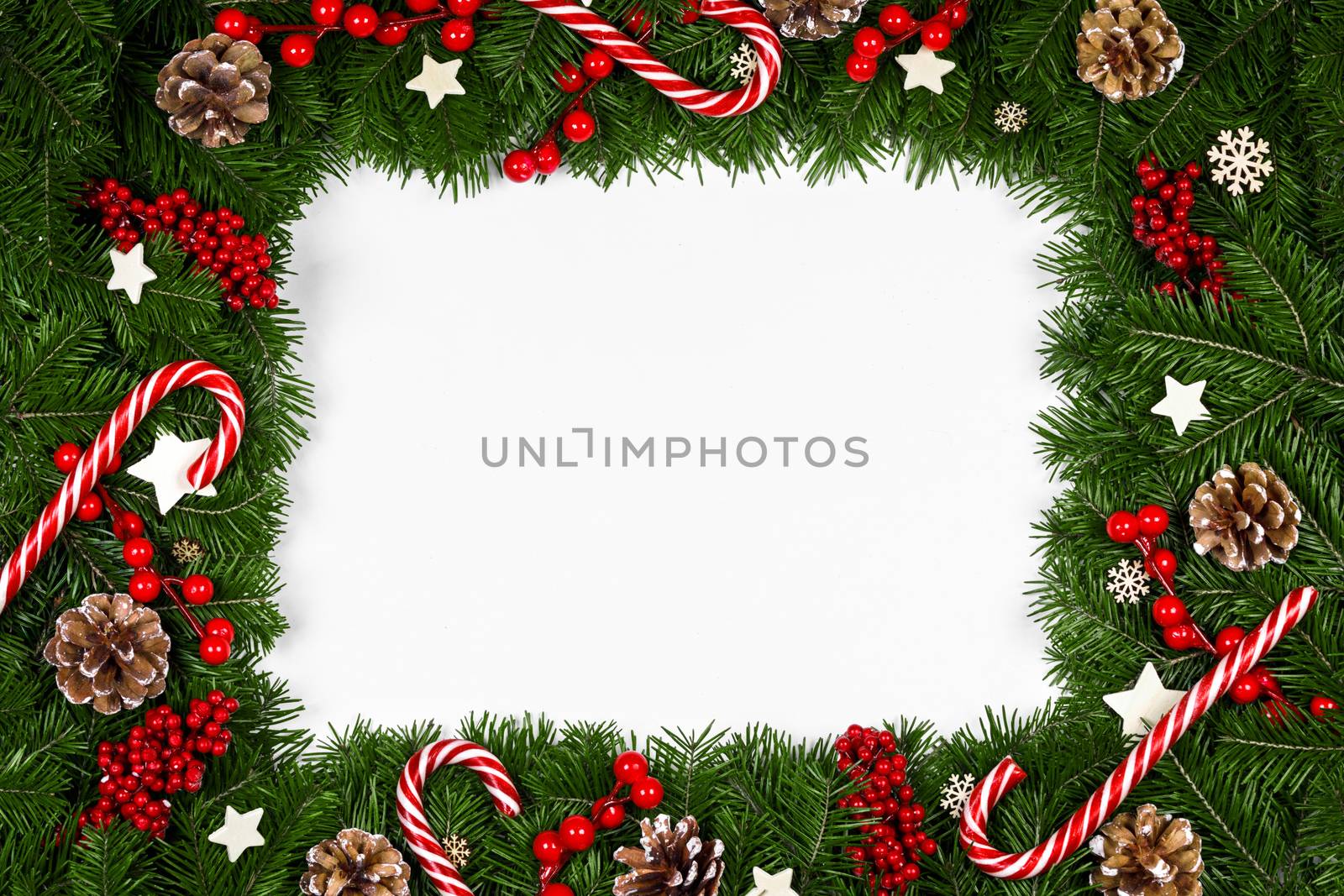 Christmas Border frame of tree branches around white background with copy space isolated, red decor, berries, stars, cones, candy canes