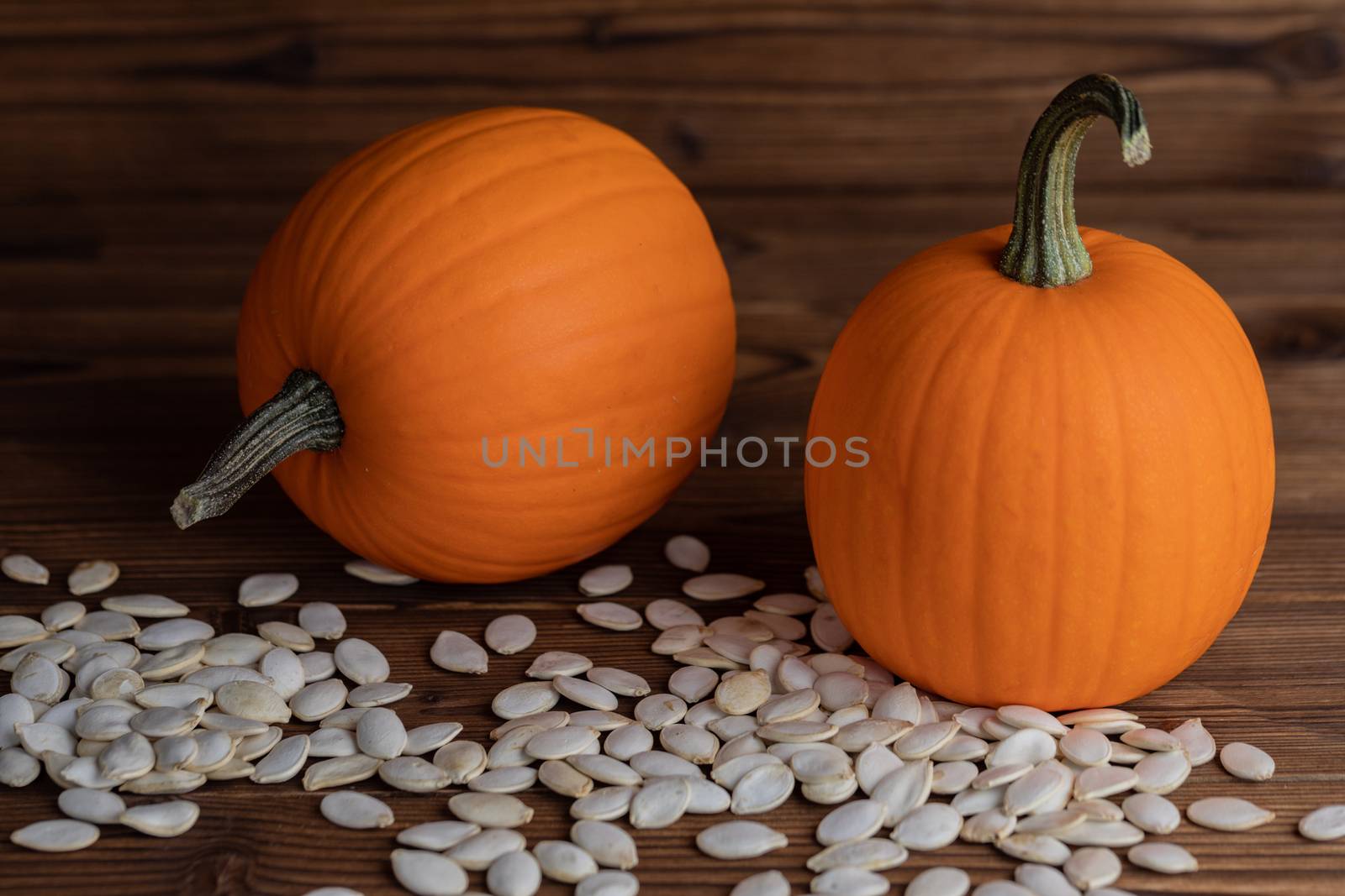 Fresh orange pumpkins and pimpkin seeds close-up on wooden background