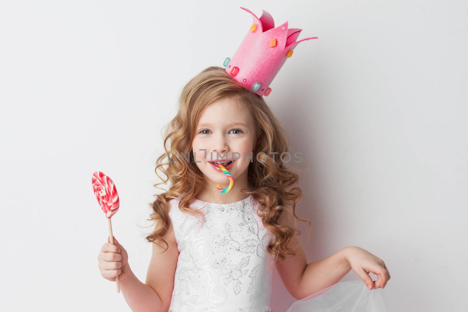 Beautiful little candy princess girl in crown holding big pink heart lollipop and candy cane