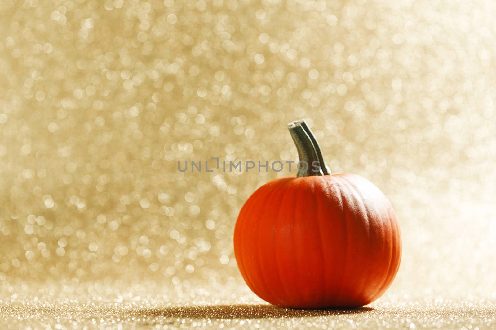 Pumpkin on golden glittery background with bokeh lights
