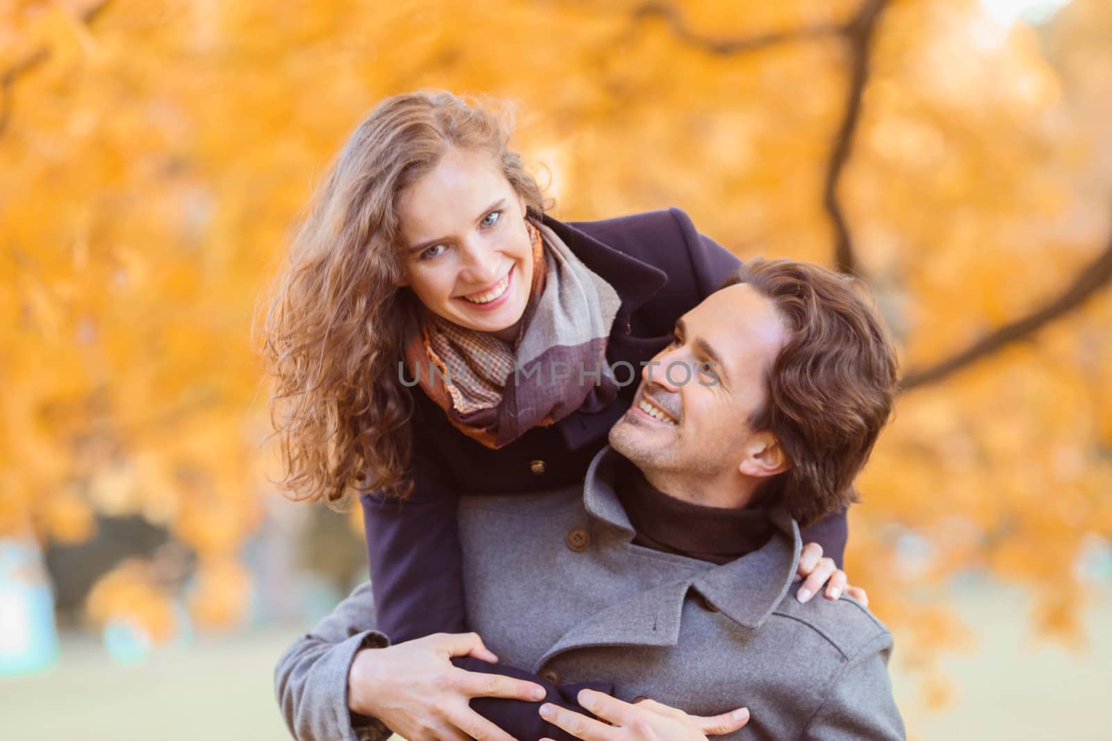 Couple in autumn park having fun, smiling man carrying woman piggyback outdoor