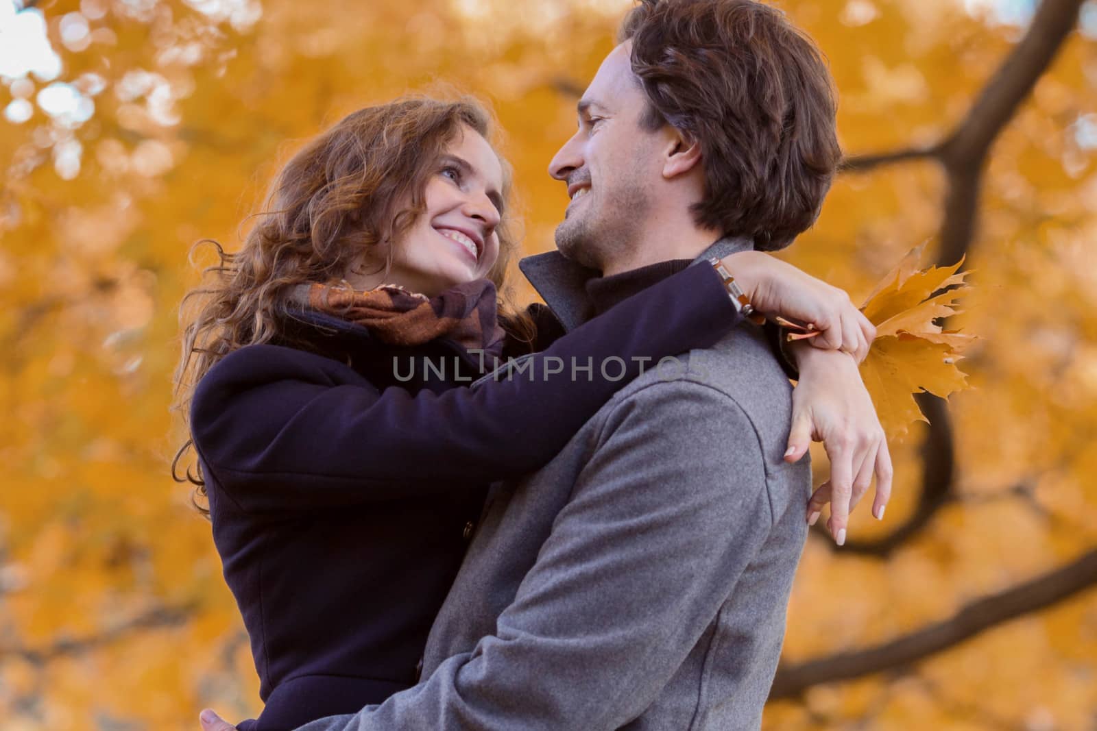 love, relationship, family and people concept - couple with maple leaves hug in autumn park