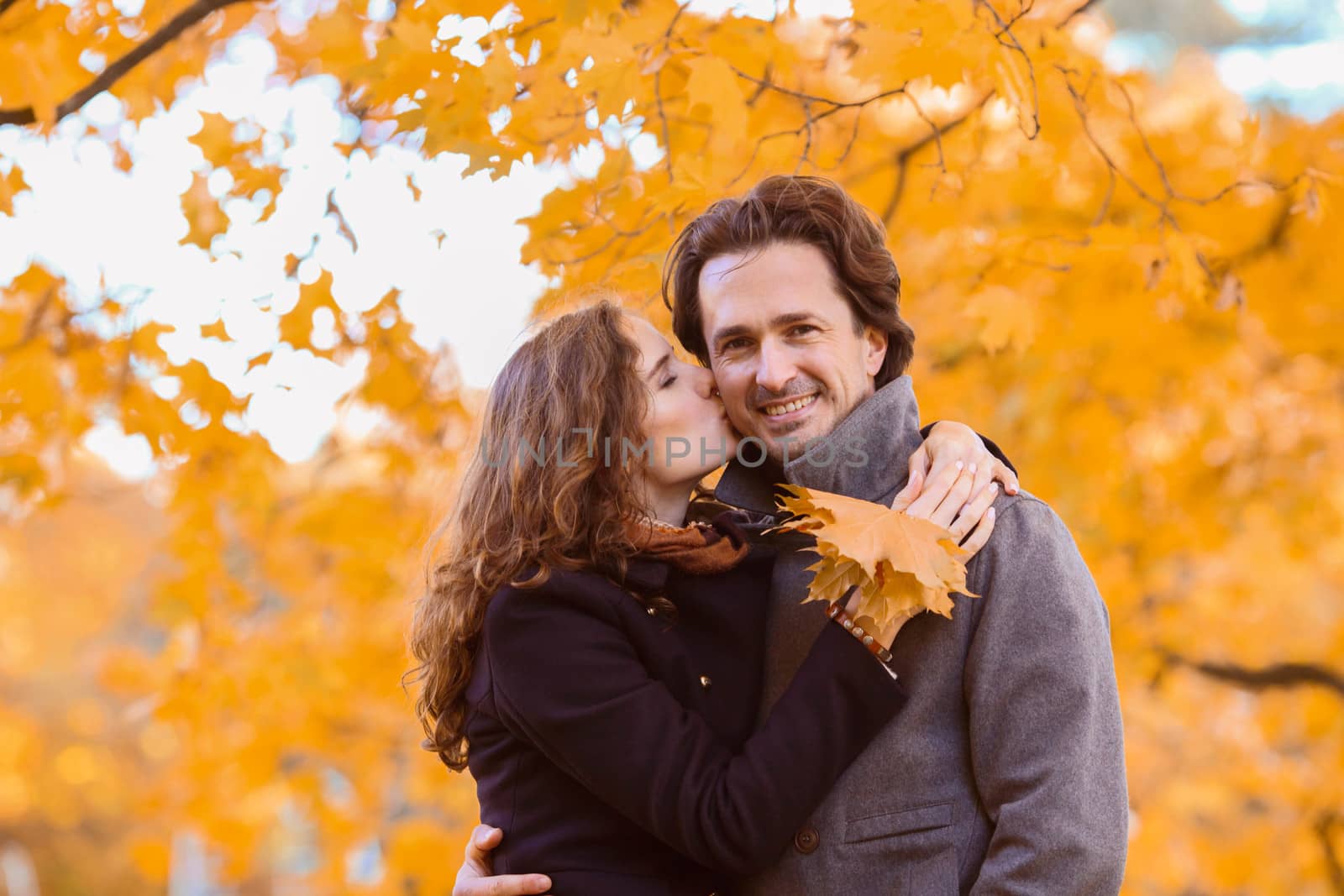 love, relationship, family and people concept - couple with maple leaves kissing in autumn park