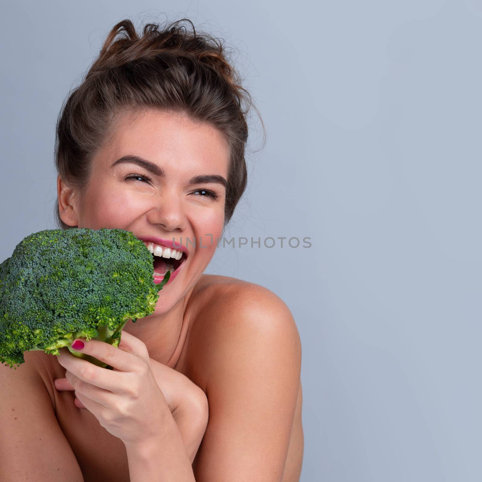 Funny happy smiling woman taking a bite out of a broccoli in a bid to eat healthily