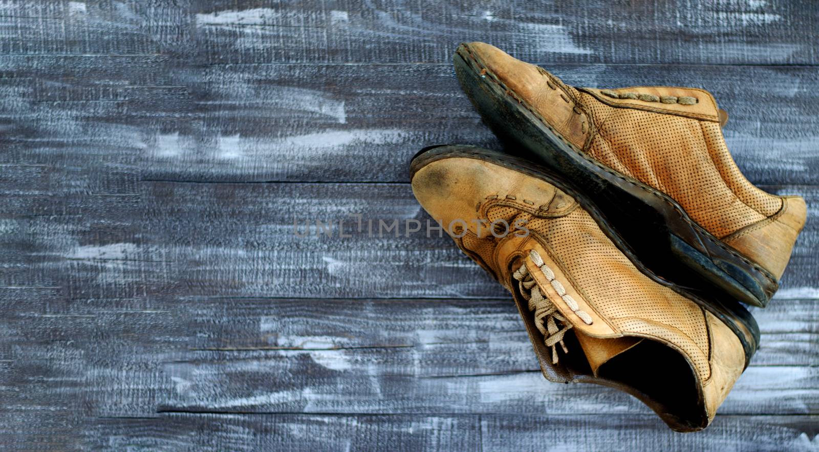 On a wooden background a pair of brown shoes. One pair of leather sneakers is very worn. Black Friday - time to buy new sneakers. Sneakers in the upper right corner are laced with laces. Close-up. Copy space.