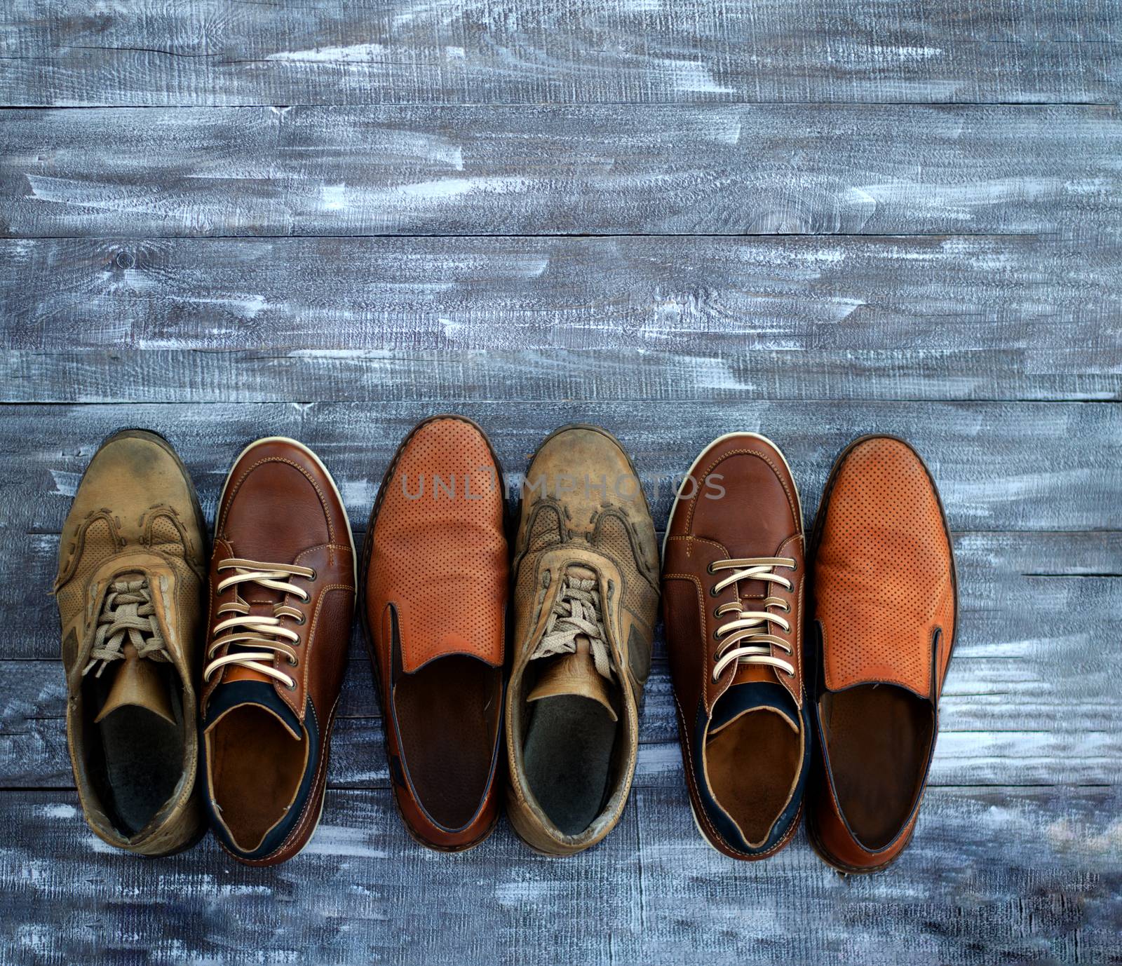 On a wooden background are three pairs of brown shoes. One pair of leather sneakers is very worn, the second is in good condition, the third pair of shoes is new. Shoes are mixed. Black Friday - time to buy new sneakers. Close-up. Copy space