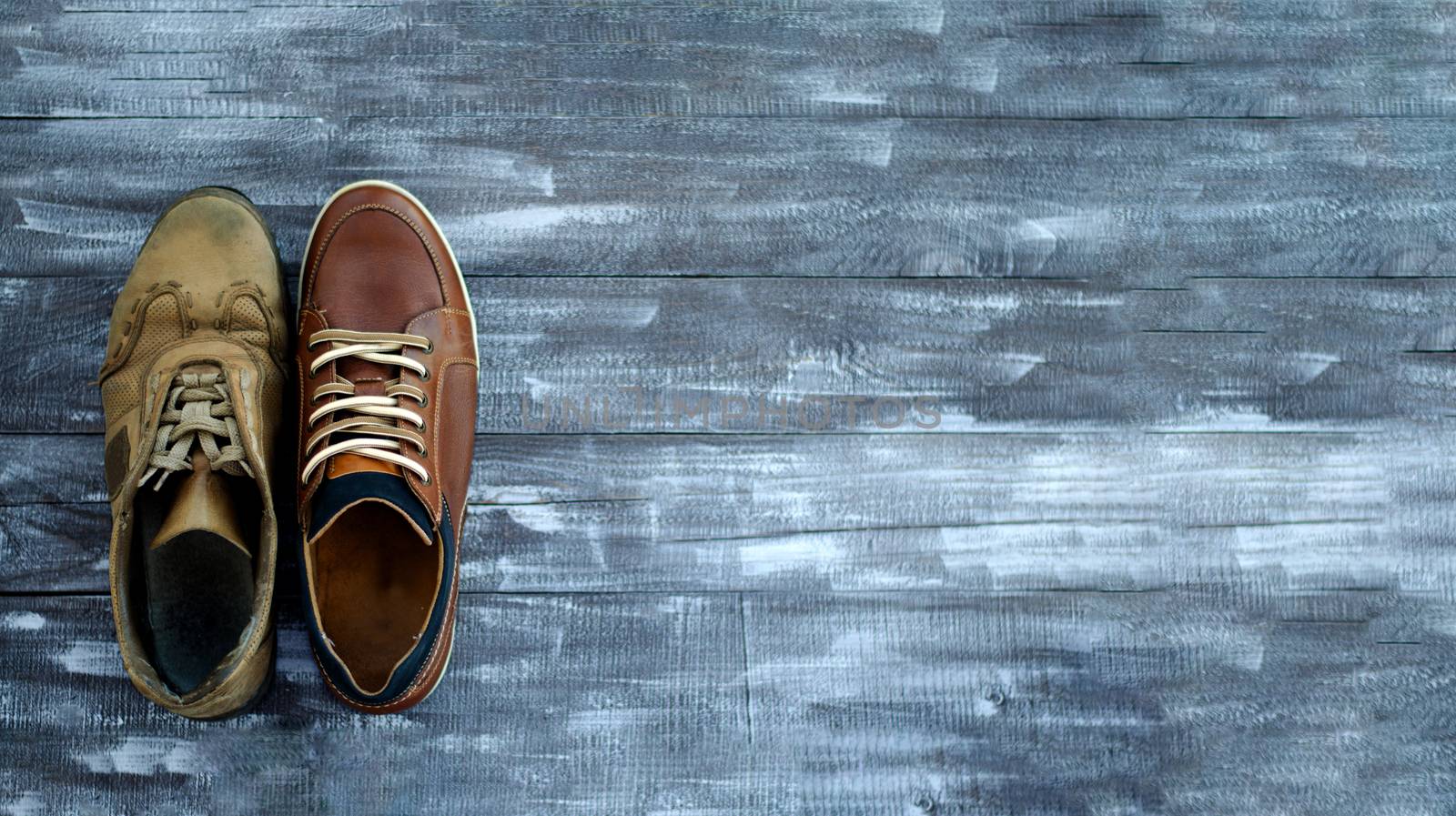 Brown shoes on a wooden background. One pair of leather sneakers, one very worn out second and new. Black Friday - time to buy new sneakers. Sneakers in the lower left corner with laces. Close-up. Copy space