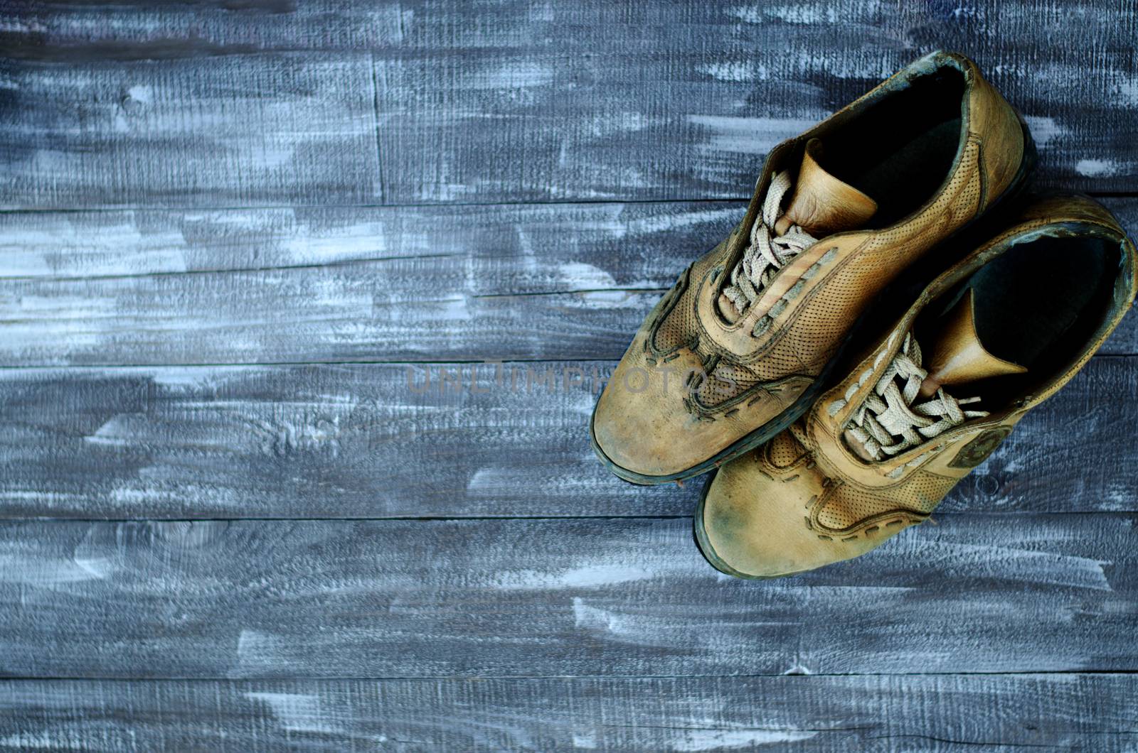 On a wooden background a pair of brown shoes. One pair of leather sneakers is very worn. Black Friday - time to buy new sneakers. Sneakers in the upper right corner are laced with laces. Close-up. Copy space.