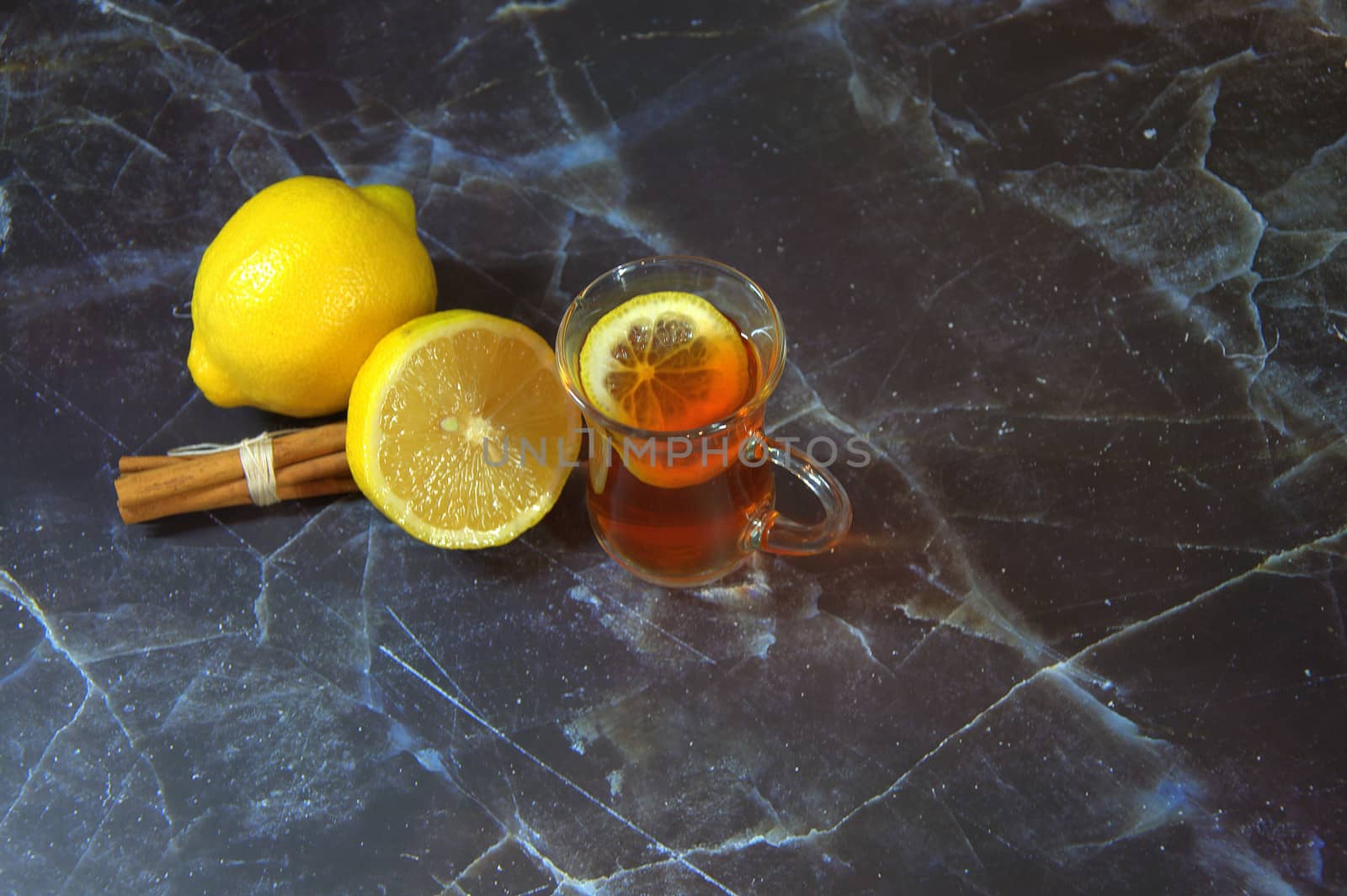 A natural cold medicine, a glass of hot tea with a slice of lemon, and next to it are cinnamon sticks and two ripe lemons. Close-up.