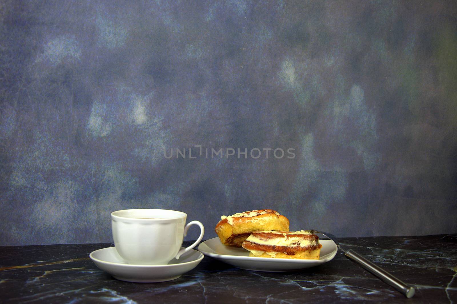 A cup of black coffee and a saucer with two fresh cinnamon rolls. Close-up.