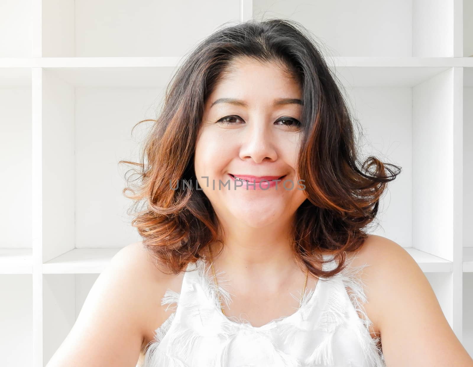 Close up portrait of a beautiful woman smiling, with white bookshelf background.
