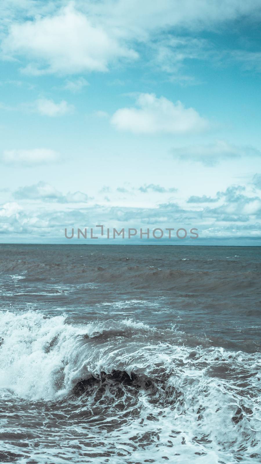 A breaking wave and stormy sea in a vertical panorama format.