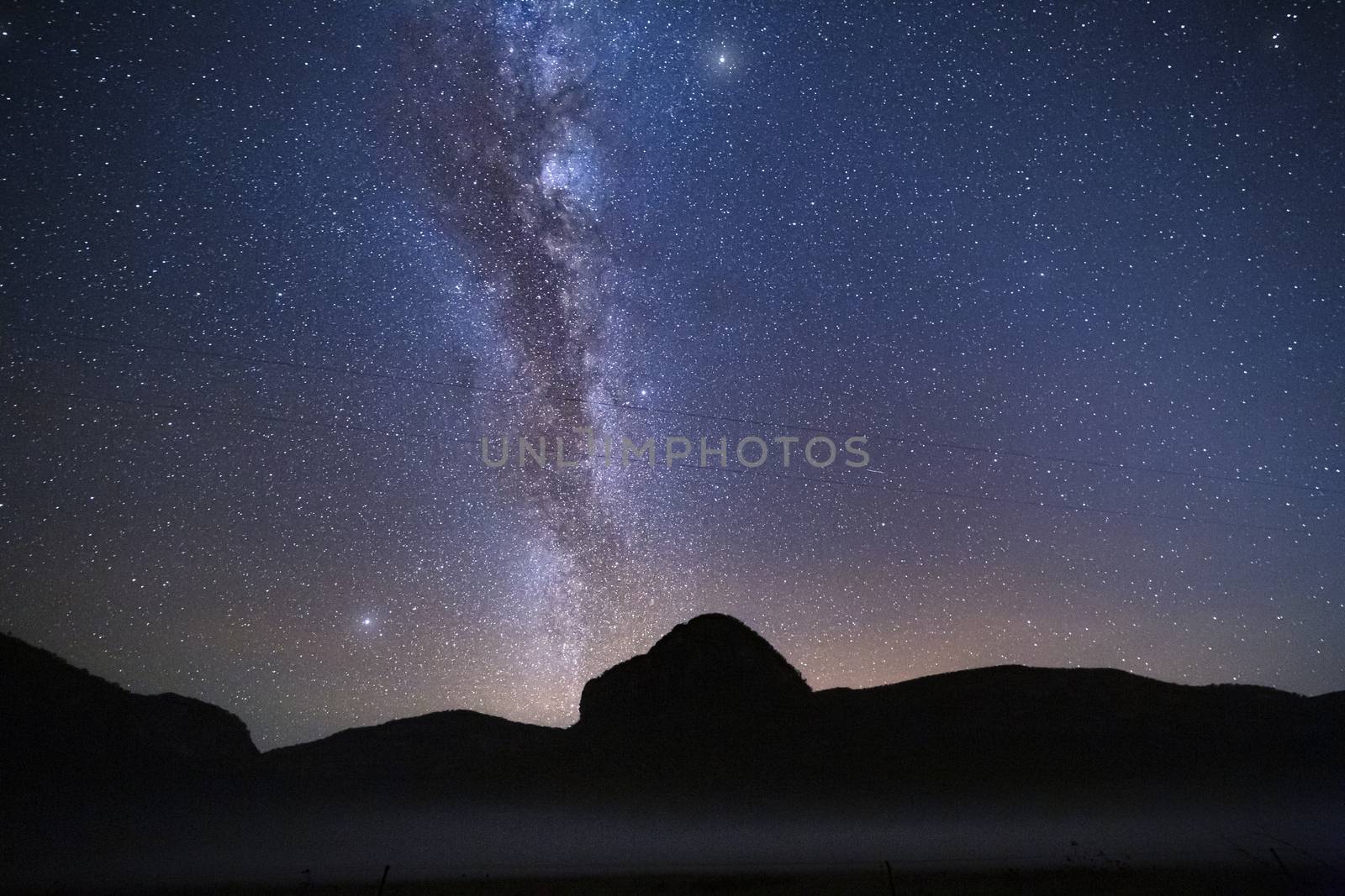 Billions of stars forming the Milky Way shining brightly overhead the Capertee Valley with a pre dawn glow on the horizon and a light mist over the land..