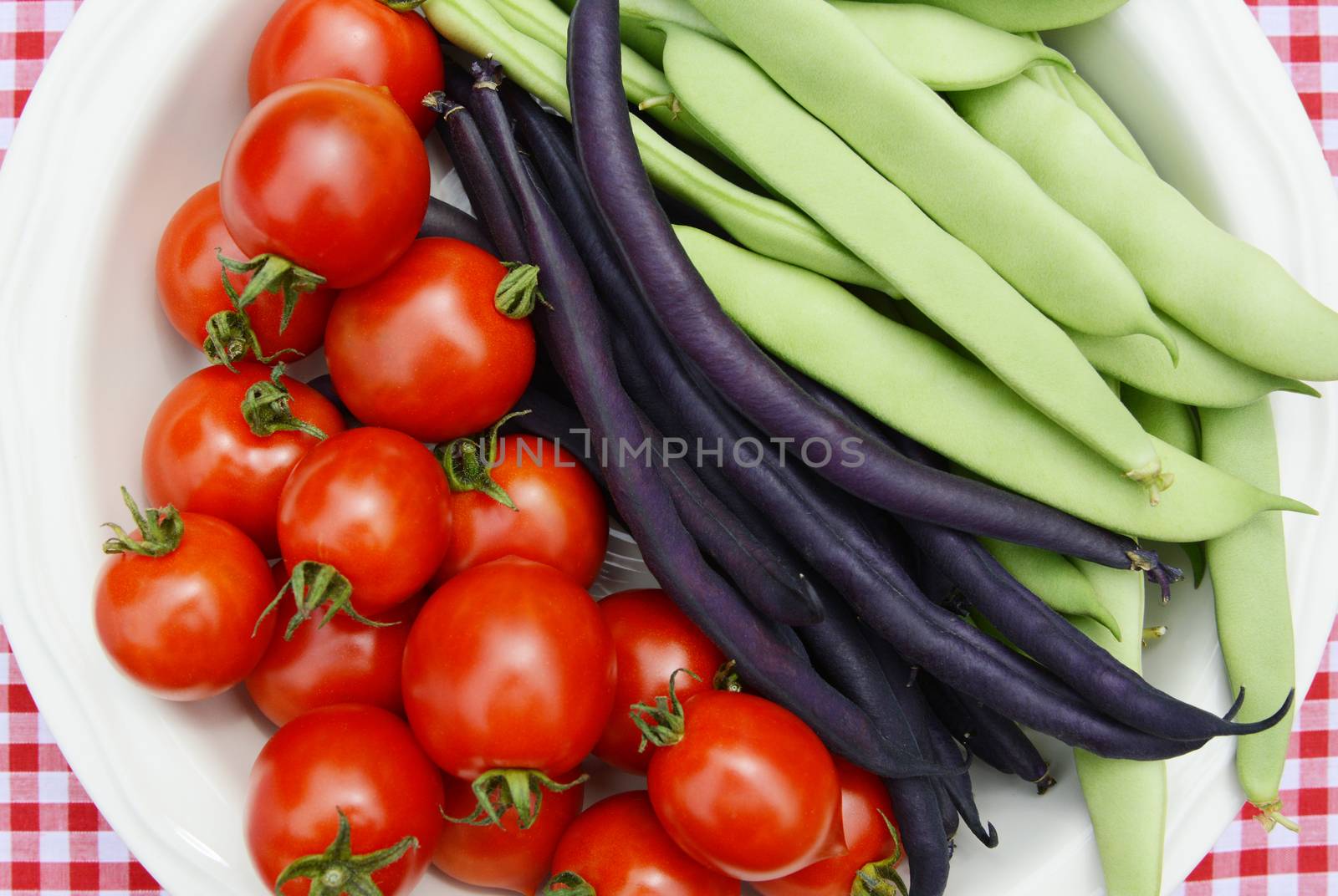 Juicy cherry tomatoes with purple French beans and green Calypso beans in a serving dish - seen from above