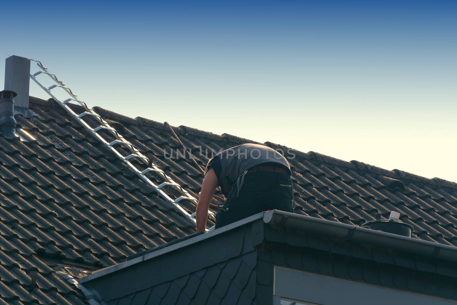 Roofer works on an unfinished roof. Installs roof shingles